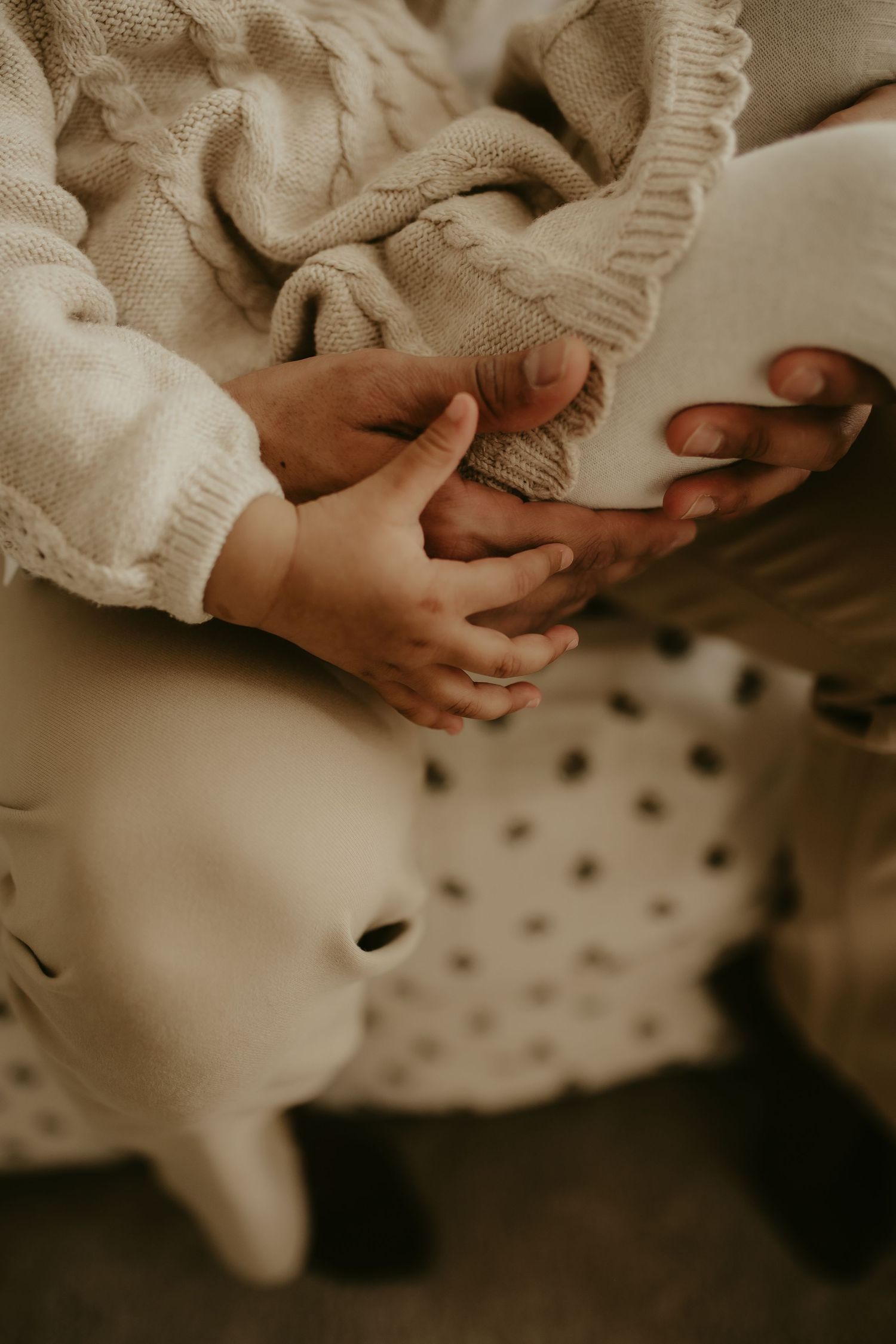 Close-up view of hands gently holding a small white bunny on a polka dot blanket in warm sepia tones.