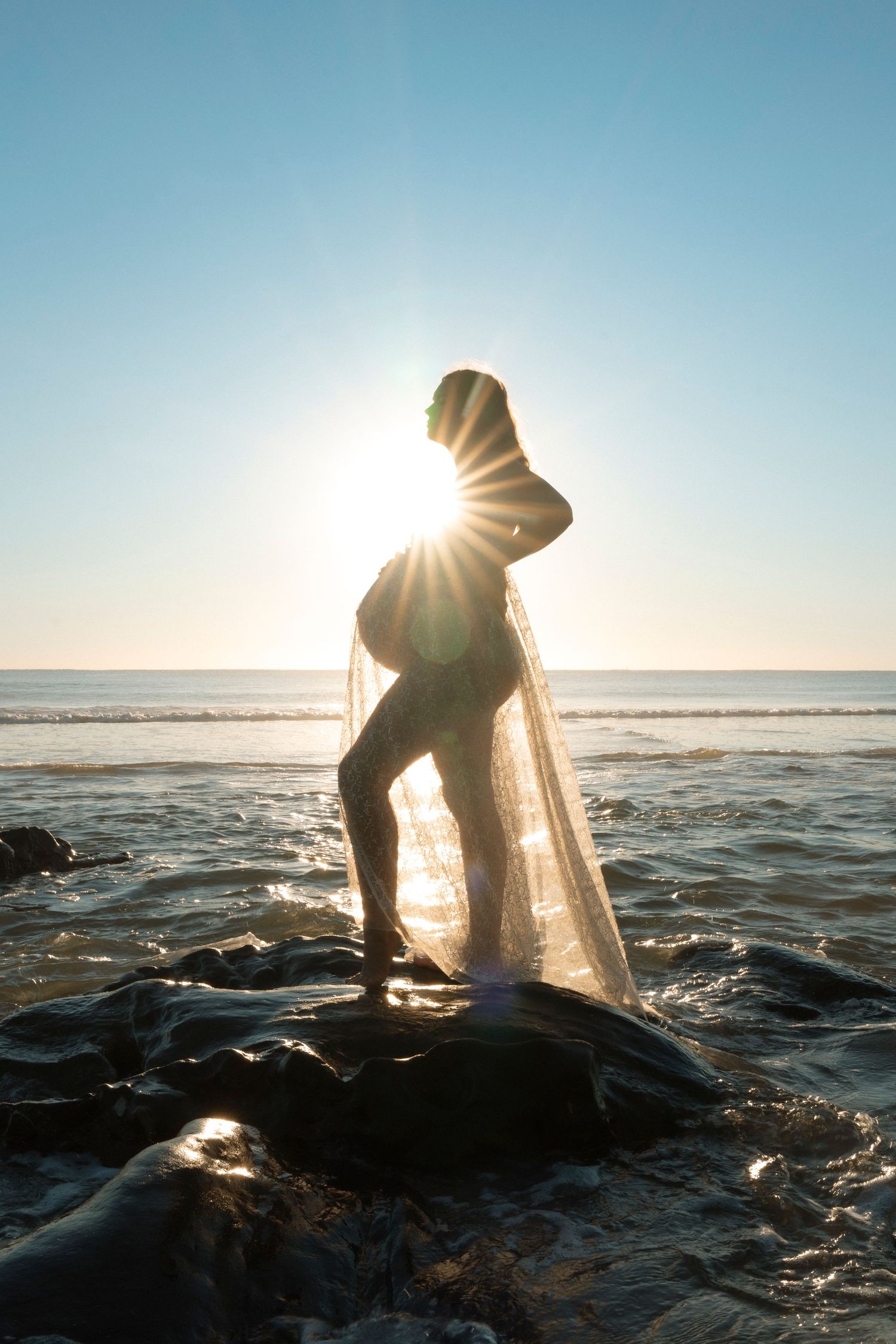 Silhouetted pregnant women with material over her belly at sunrise at the beach