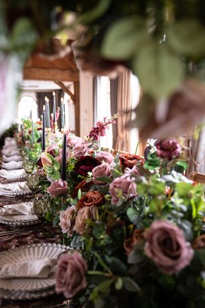 Elegant table setting with mauve roses and greenery centerpieces alongside black taper candles and ornate place settings.