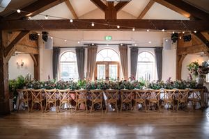 Large rustic wedding reception venue with exposed wooden beams and elegant white decor features multiple dining tables.