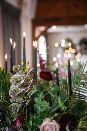 Wedding reception table centerpiece features elegant greenery and roses with decorative spiral accents in warm lighting.