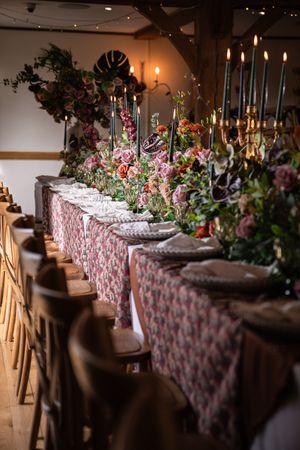 Long banquet table decorated with floral arrangements and pink patterned tablecloth for elegant wedding reception.