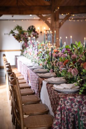 Elegant wedding reception table settings with floral tablecloths, rustic chairs, and soft candlelight create a romantic atmosphere.