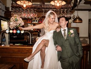 A bride and groom share intimate moments in a rustic bar setting with warm lighting and hanging glassware.