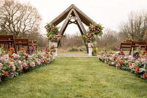 Wooden wedding arch decorated with pink and white flowers stands at the end of an aisle lined with floral arrangements.