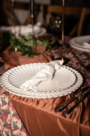 White decorative plate with folded napkin on brown tablecloth at elegant table setting.