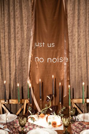 Elegant wedding reception table decorated with multiple lit taper candles and floral arrangements against a draped fabric backdrop.