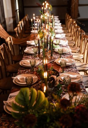 Elegant rustic dining table set with glowing candles, rose gold plates, and tropical greenery for a romantic reception.