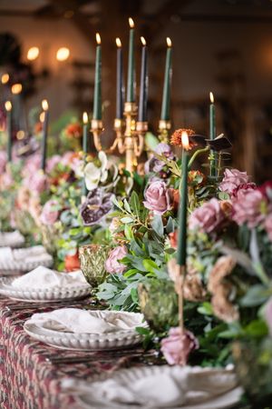 Elegant table setting with white plates, lit candles, and pink floral arrangements creating a romantic dining atmosphere.