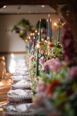 Elegant table setting with tall green candles and pink floral arrangements along a formal dining table with crystal glassware.