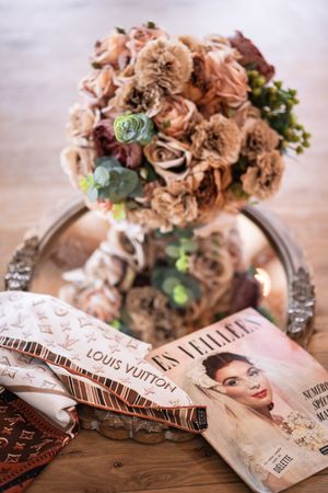 Dried floral arrangements displayed alongside scattered fashion magazines and Louis Vuitton publications on a wooden surface.