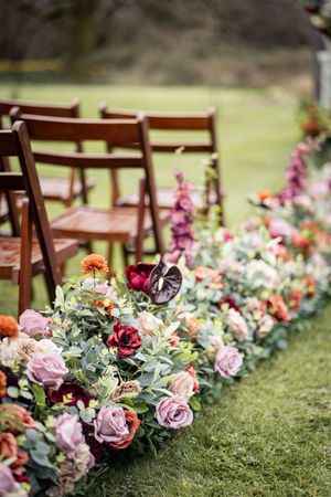 Beautiful floral aisle decorations with pink roses and wooden chairs set up for an outdoor garden wedding ceremony.