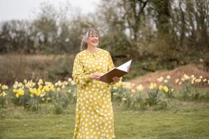 Woman in yellow polka dot dress twirls joyfully in a field of spring daffodils on a sunny day.