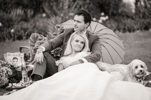 A romantic black and white engagement photo series showing a couple lying in grass with their dog.