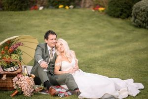 A romantic couple in wedding attire relaxes together on a lush green lawn during their outdoor photoshoot.