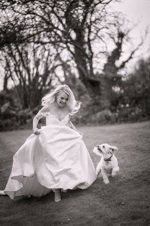 A black and white sequence of a bride in a flowing white dress rolling down a grassy hill in playful motion.