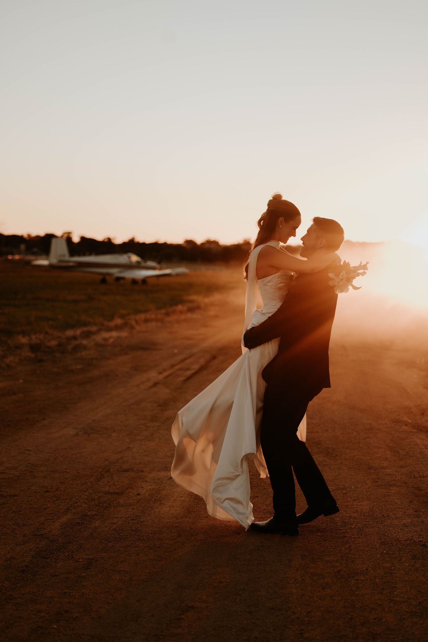 Black and white photo of a bride and groom sharing a romantic moment at sunset on a rural road.