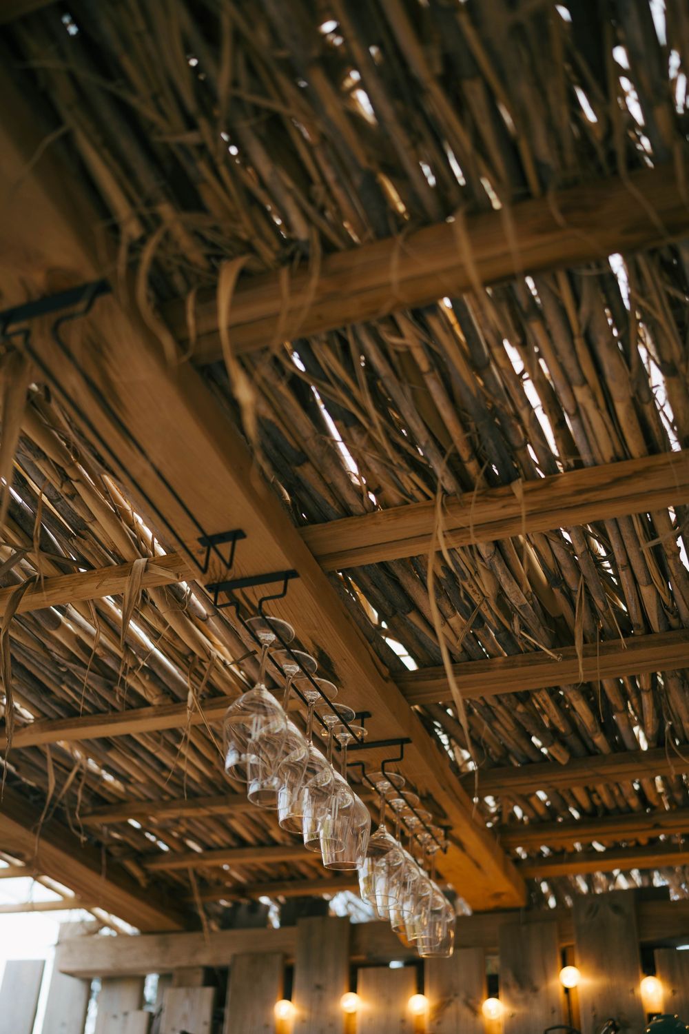 Rustic wooden ceiling with exposed beams, hanging wine glasses, and warm Edison bulb lighting in a bar.