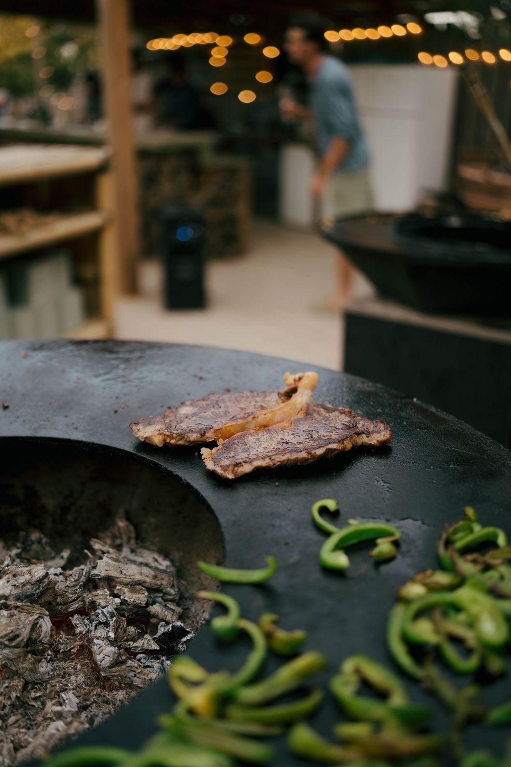 Viande grillée et poivrons verts cuits sur une grande plaque chauffante en fer extérieure au-dessus de charbons ouverts dans un restaurant d