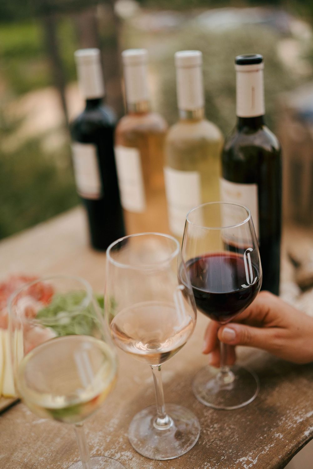 Une main tenant un verre de vin rouge lors d'une dégustation de vin en plein air avec des verres et des bouteilles de vin blanc