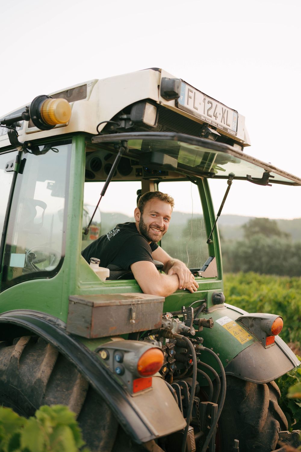 Smiling farmer sitting in a green tractor in a vineyard field on a sunny day.