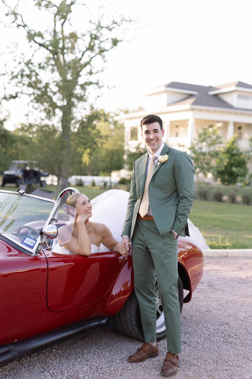 A romantic moment captured with a couple and a vintage red convertible car on a gravel driveway.