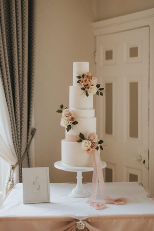 Elegant four-tier white wedding cake decorated with blush roses and greenery on a pedestal at Cave Castle - taken by Grimsby photographer.