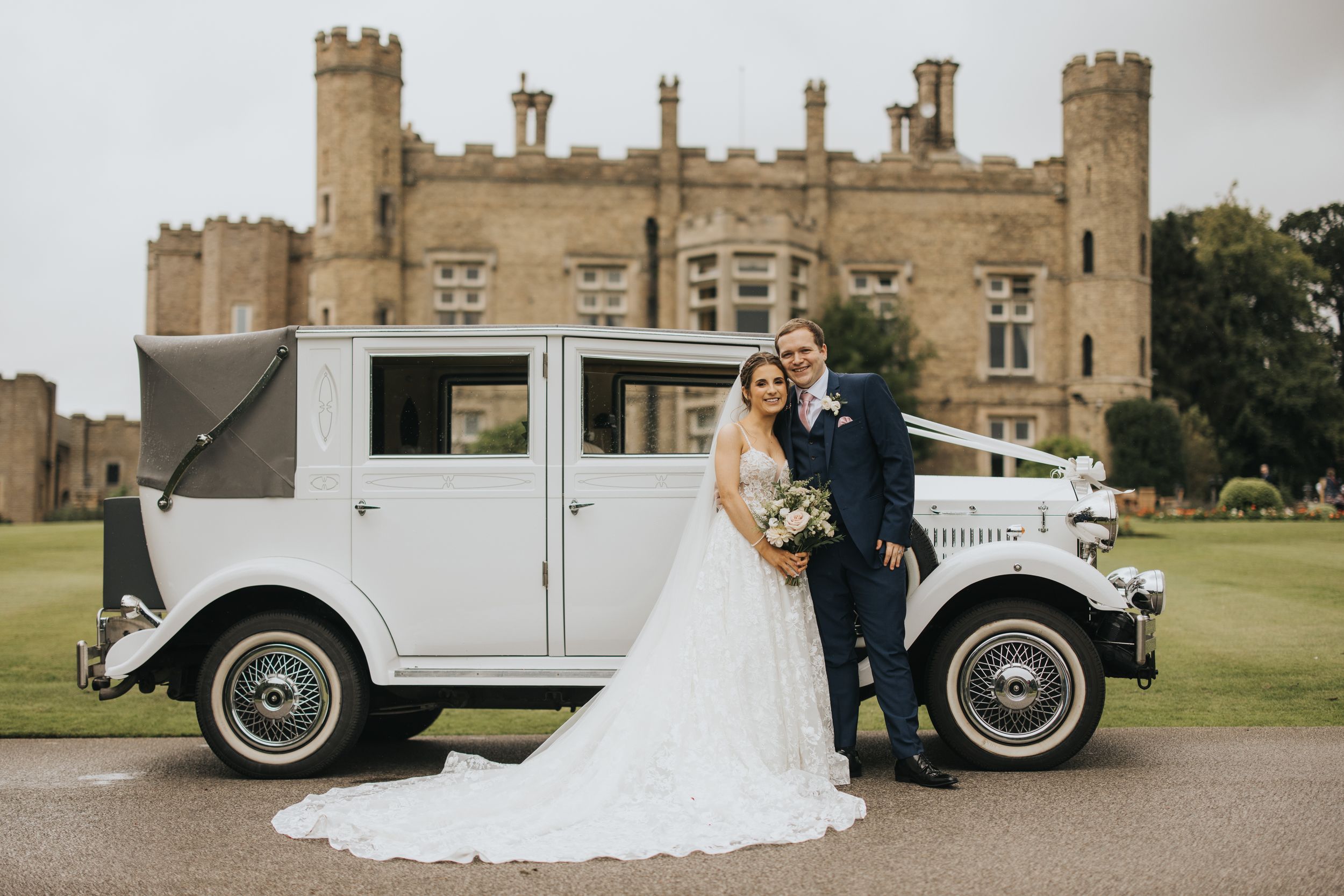 A couple poses with a vintage white wedding car in front of Cave Castle - taken by Grimsby photographer.