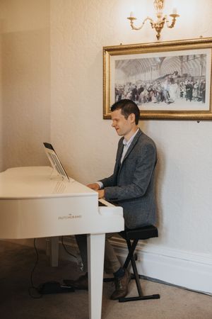 A pianist is seated at a white grand piano in a minimalist room with framed artwork on the wall at Cave Castle - by Grimsby photographers.