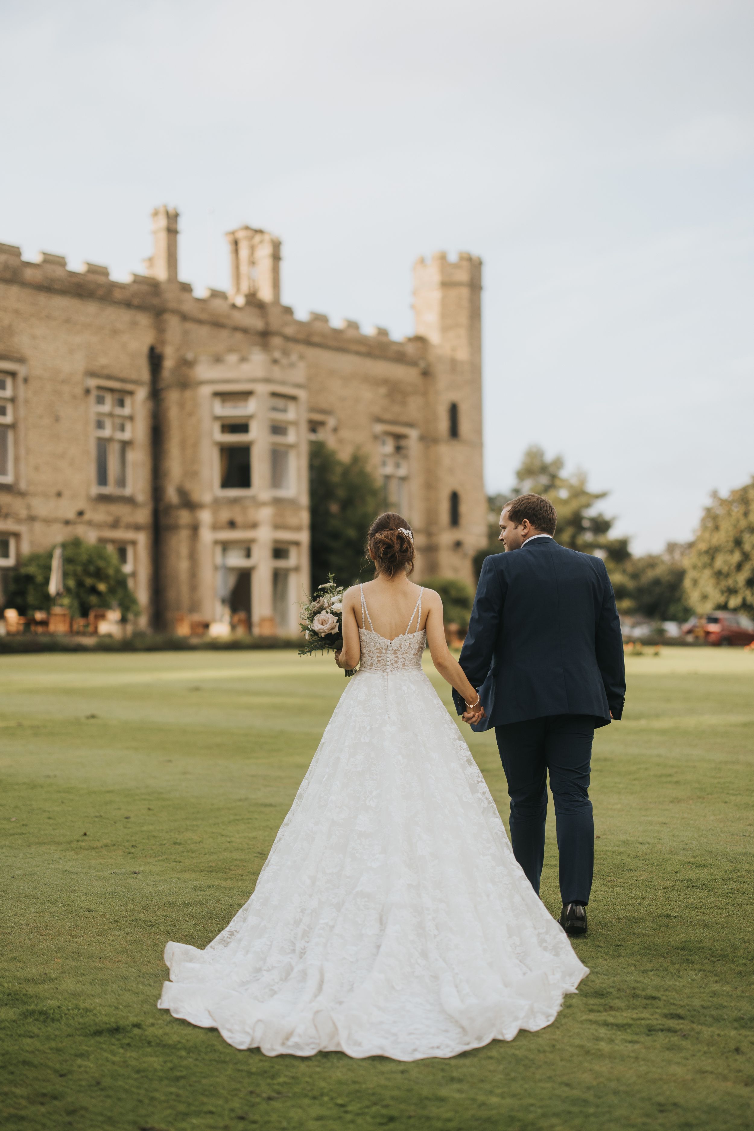 A couple in wedding attire walks across a pristine lawn towards Cave Castle - taken by Grimsby photographer.