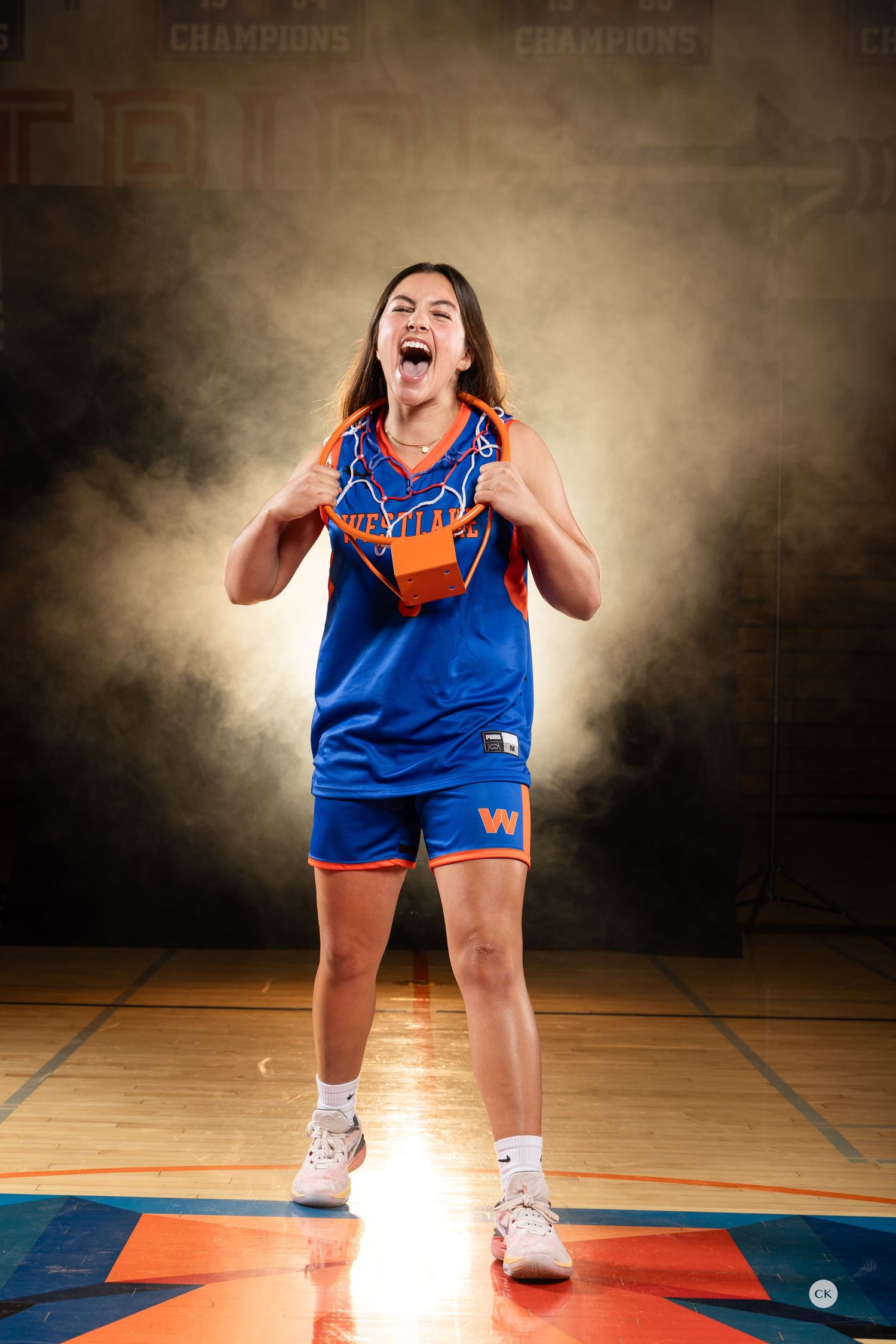 Basketball player in blue and orange uniform shows intense emotion on court with dramatic lighting.