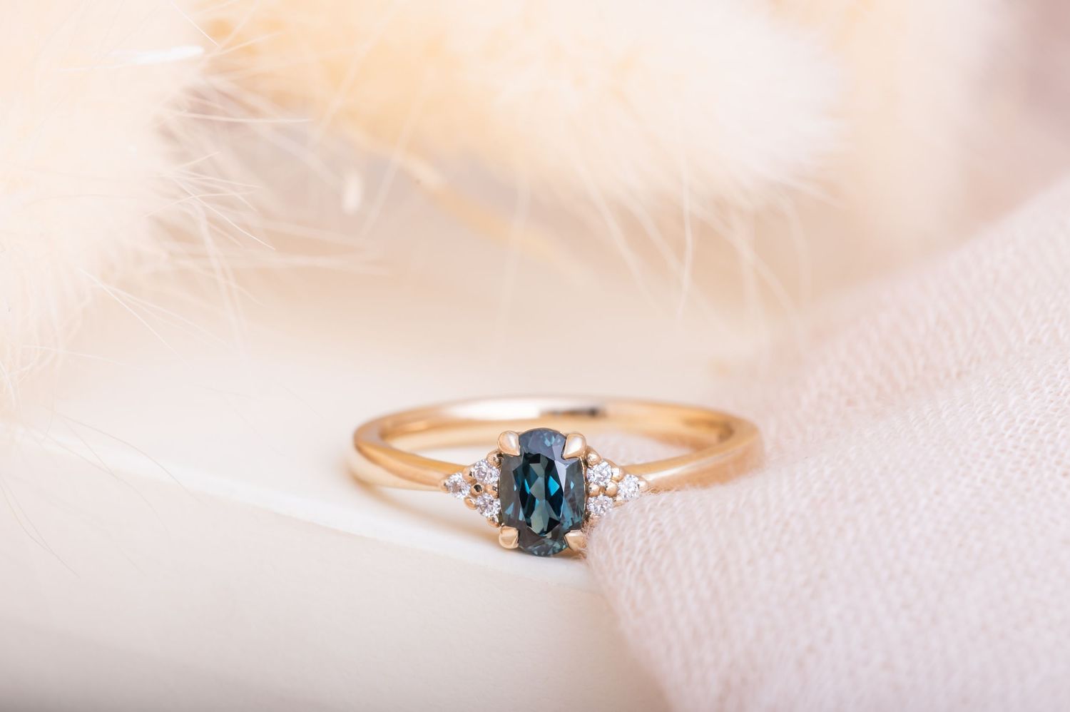 Delicate rose gold ring with teal gemstone and diamonds photographed on soft fabric.
