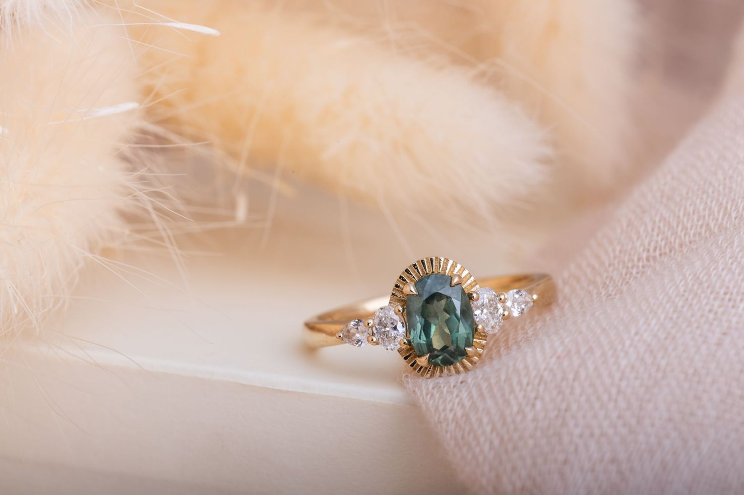 Ethereal photo of a teal gemstone ring with diamond accents on soft beige fabric.