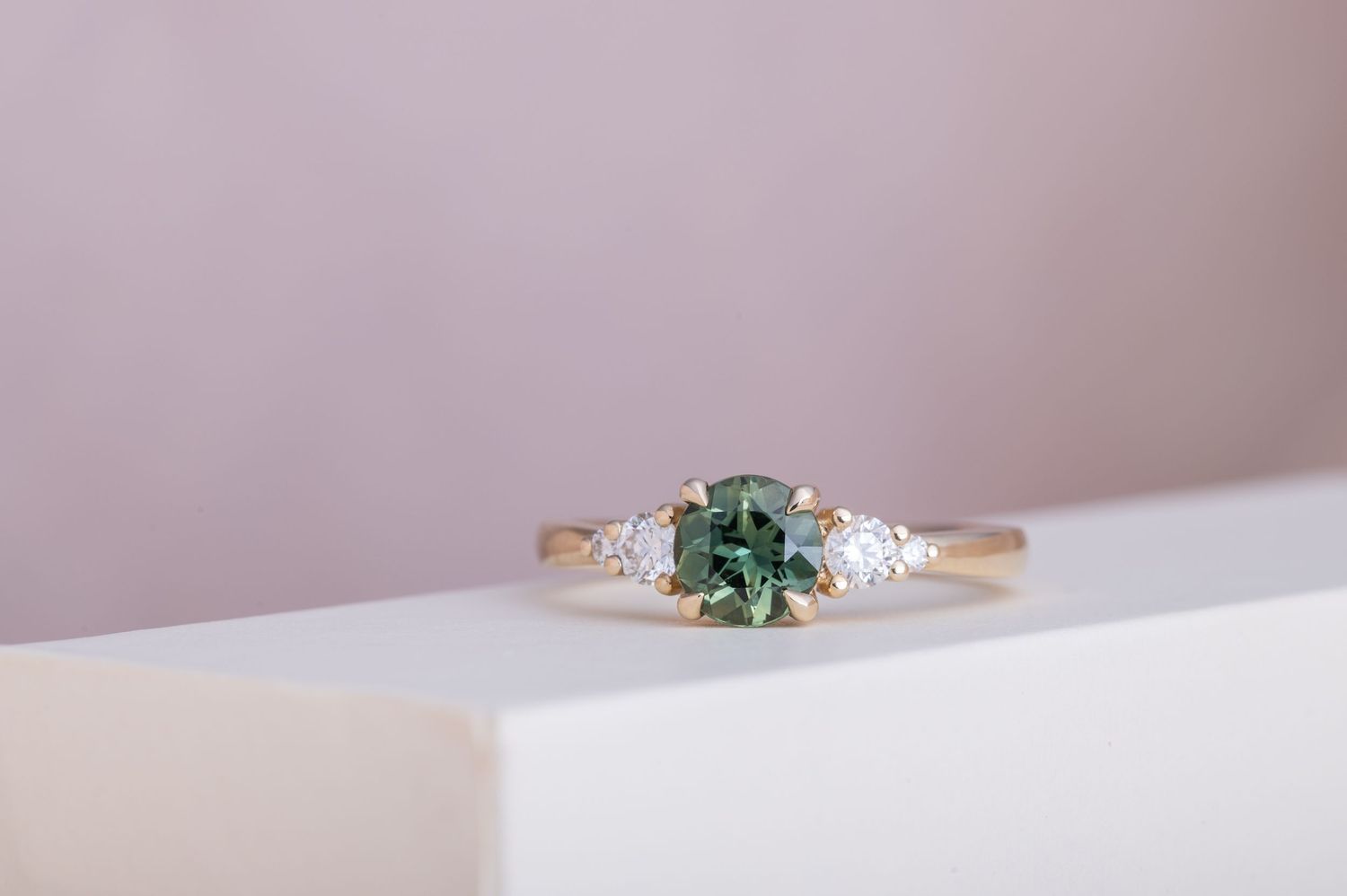 Dainty engagement ring featuring a green-blue center stone and diamond side stones.