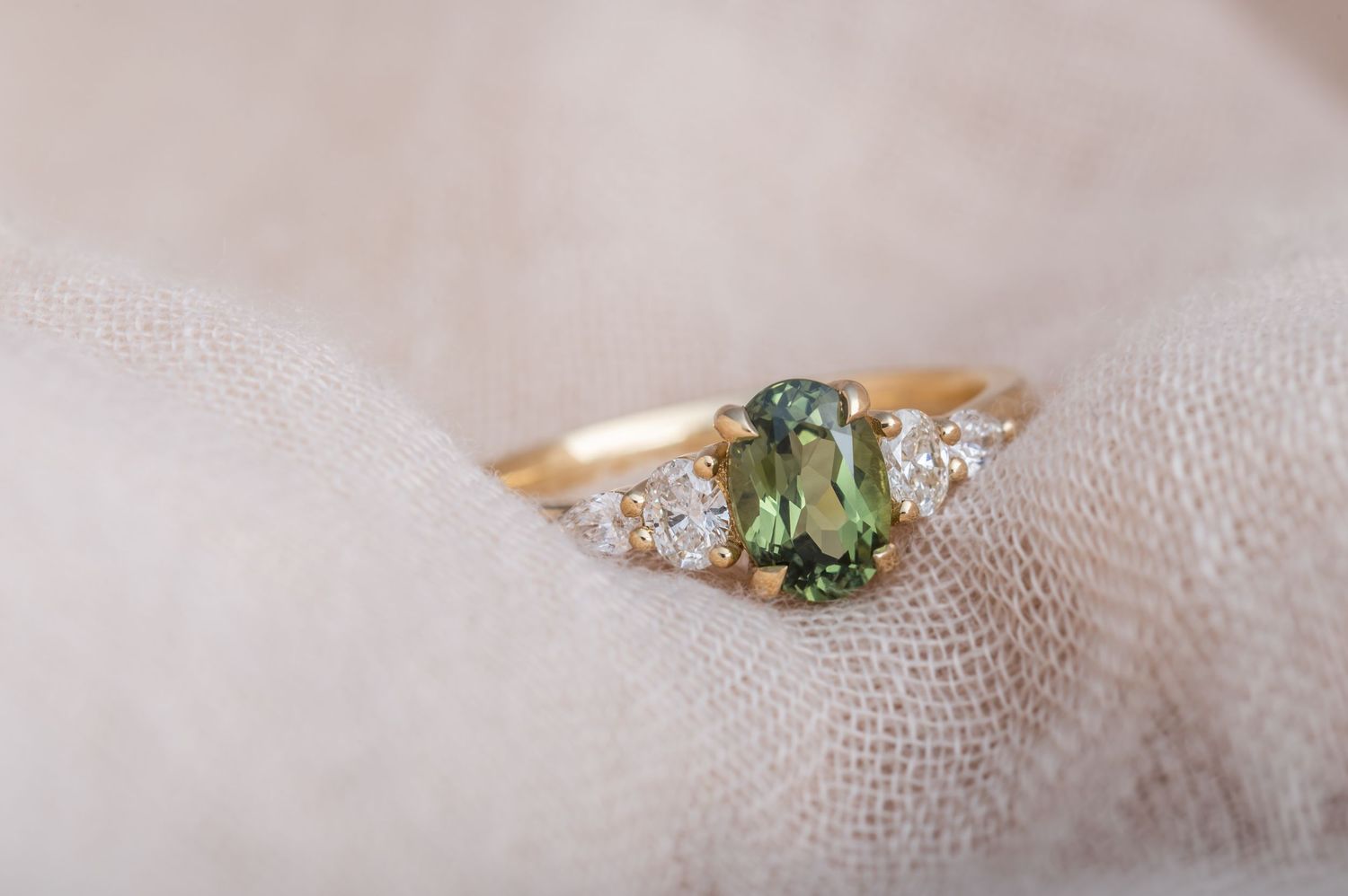 Close-up photos of delicate gold rings with gemstones on a textured fabric background.