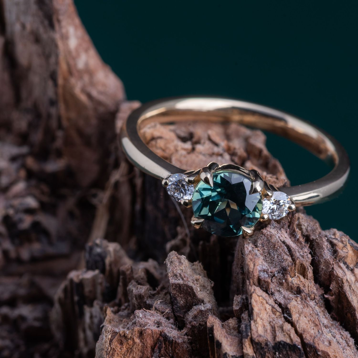 Detailed shot of teal gemstone ring with diamond accents against dark background.
