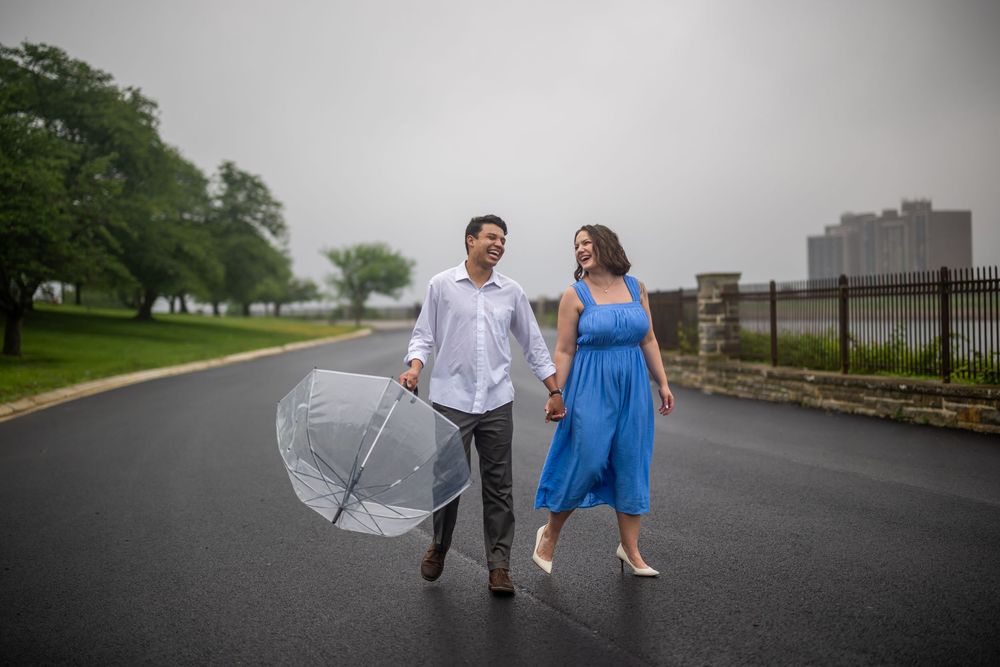 Two people walking together in the rain on a cloudy day, with one holding a clear umbrella, in baltimore Druid Hill Park.