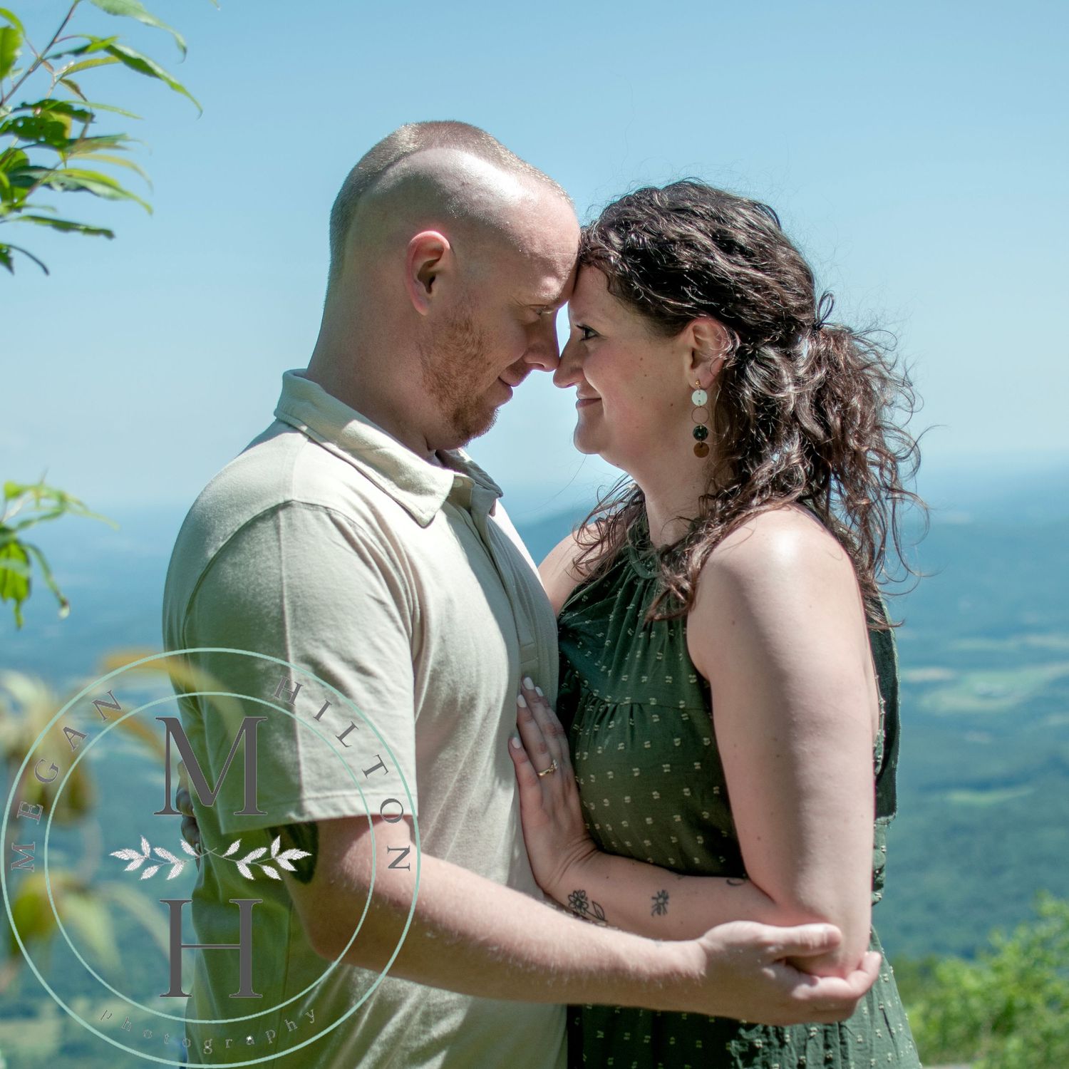 A couple holds each other lovingly in front of mountain scenery on a sunny day overlooking the Shenandoah Mountain valley.