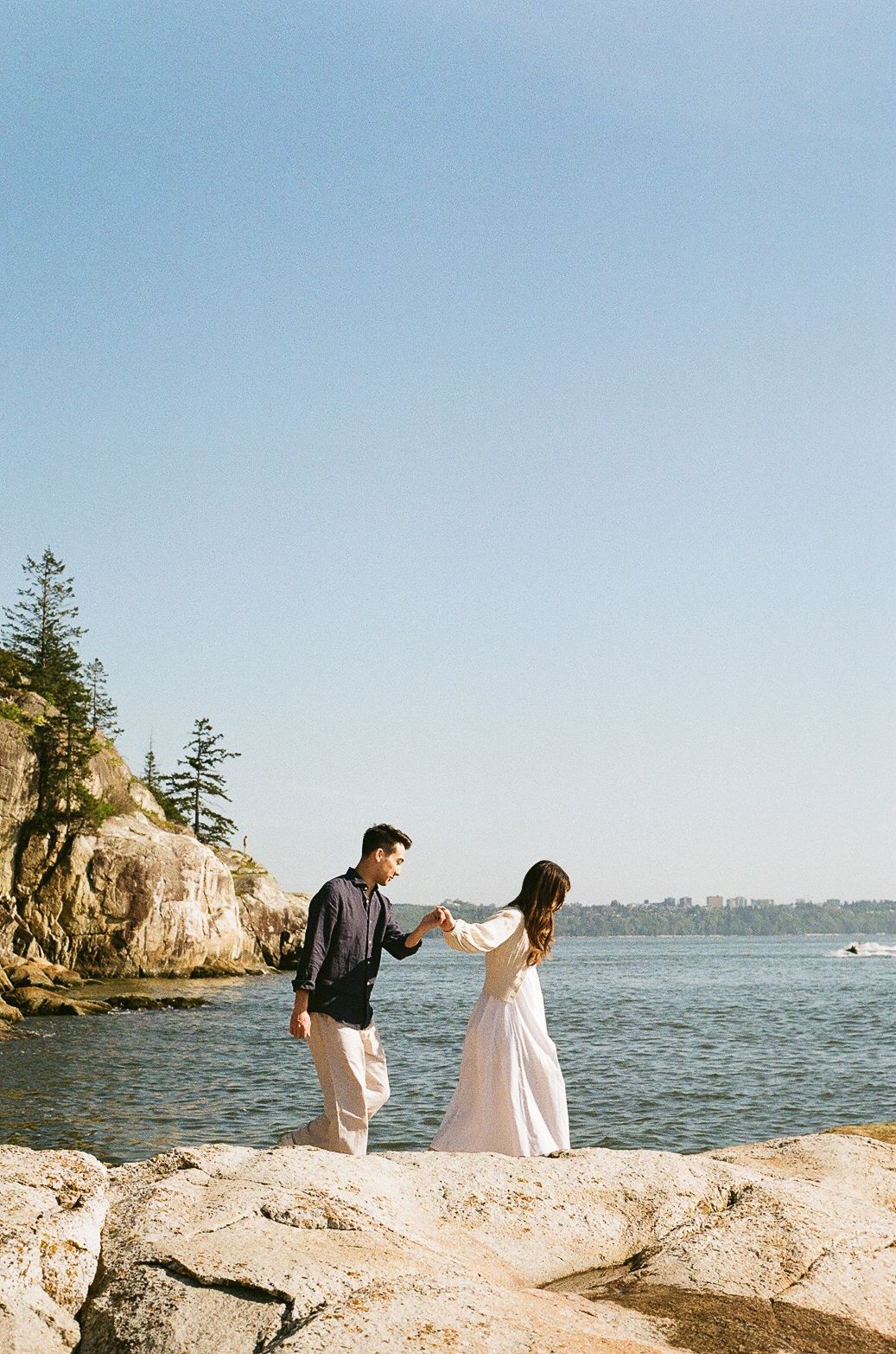 Couple walking along rocky coastal cliffs overlooking a scenic ocean bay.