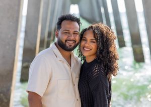 Couple in casual attire pose together under architectural columns outdoors.