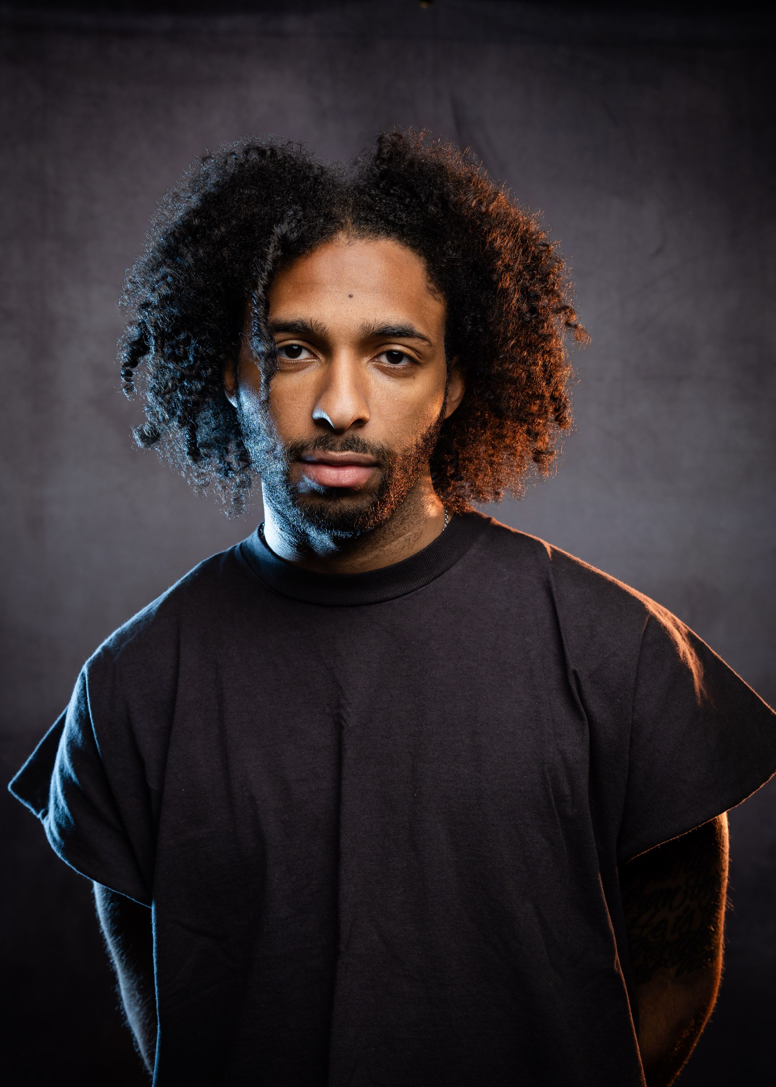 A person wearing black clothing poses with curly hair against a dark background in a photo series.