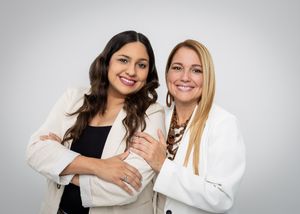 Two women in white blazers pose together in professional studio portrait.