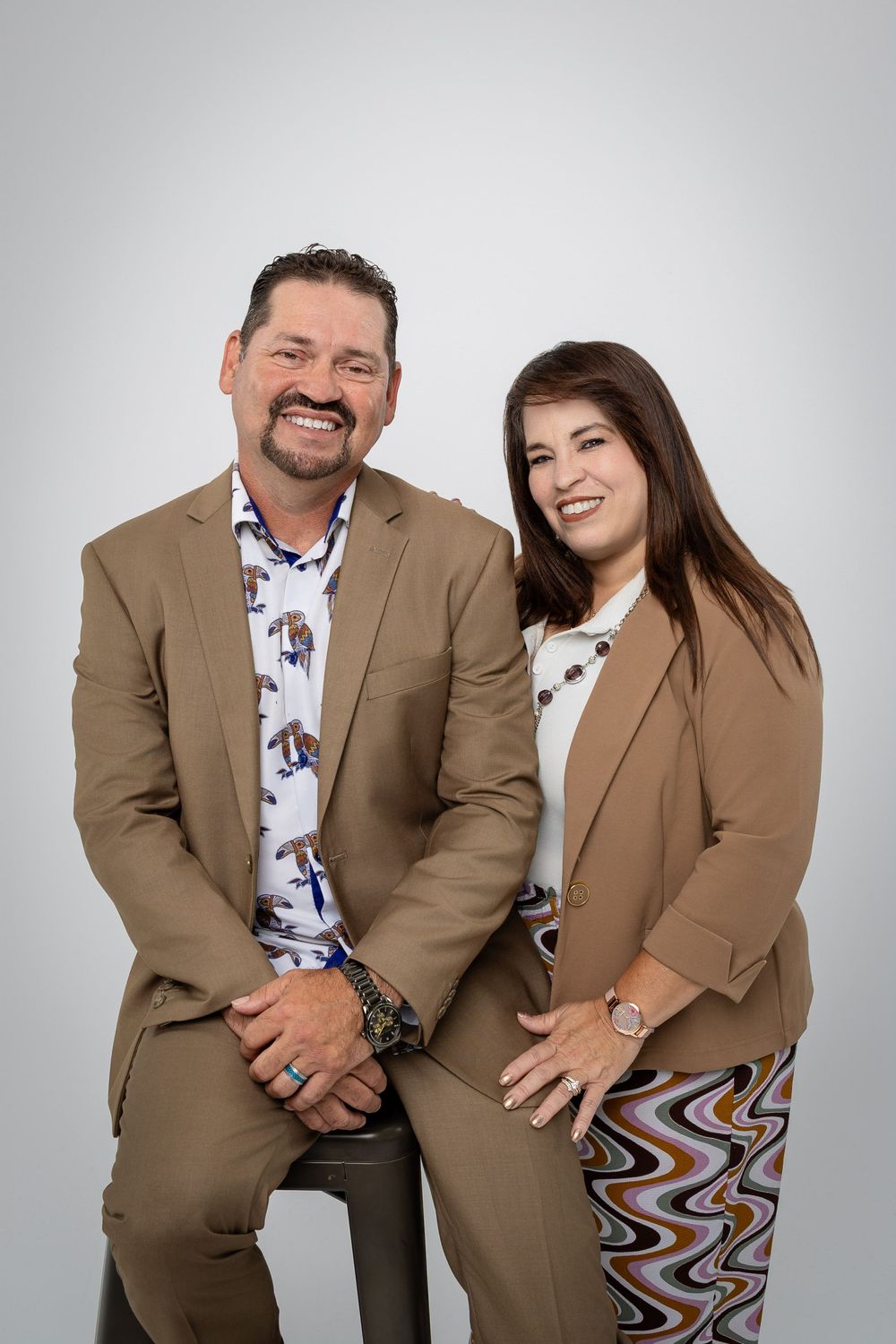 Professional couple portrait series in matching brown suits against light studio backdrop.