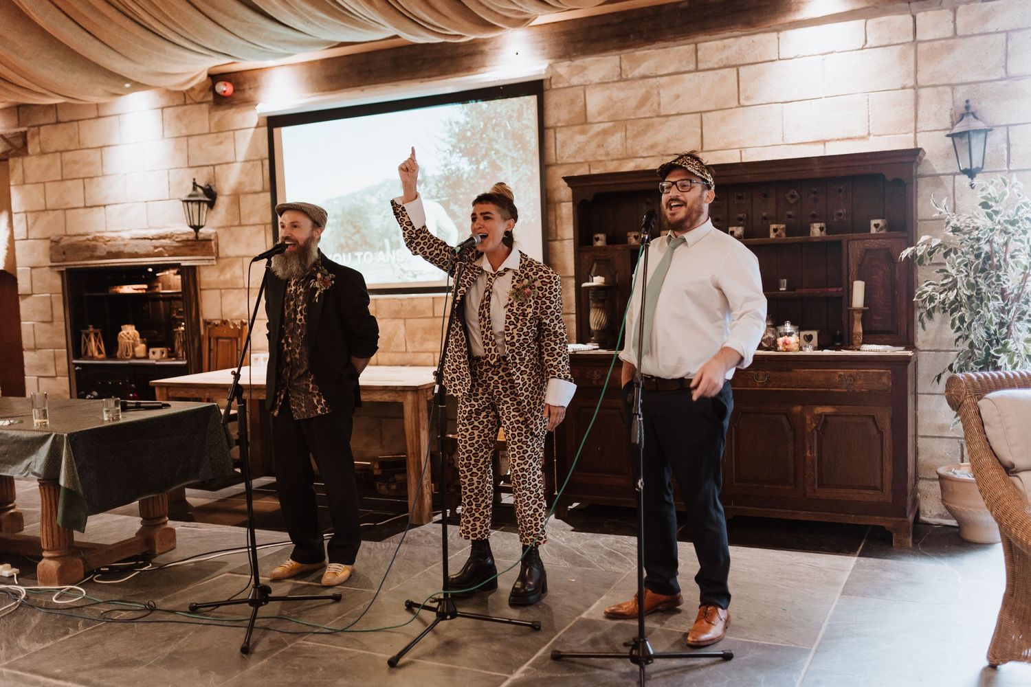 Three performers stand at microphones singing together in what appears to be a historic church or chapel interior.
