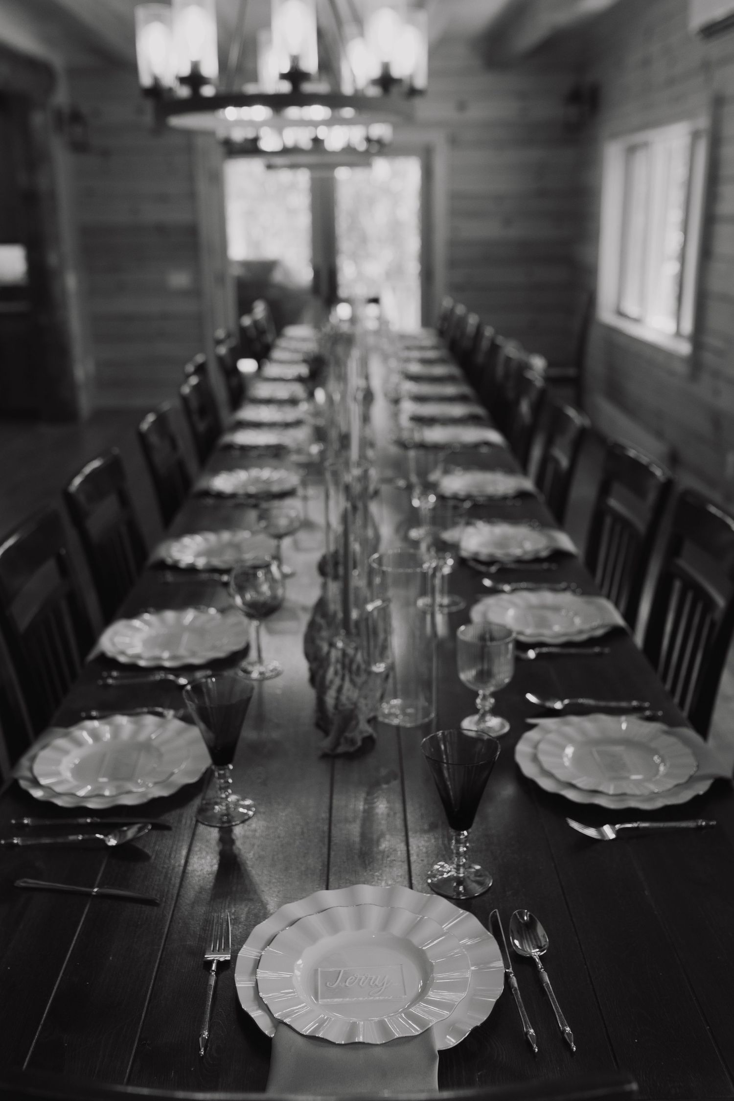 A long rustic dining table set with elegant white plates and wine glasses in a log cabin dining room.
