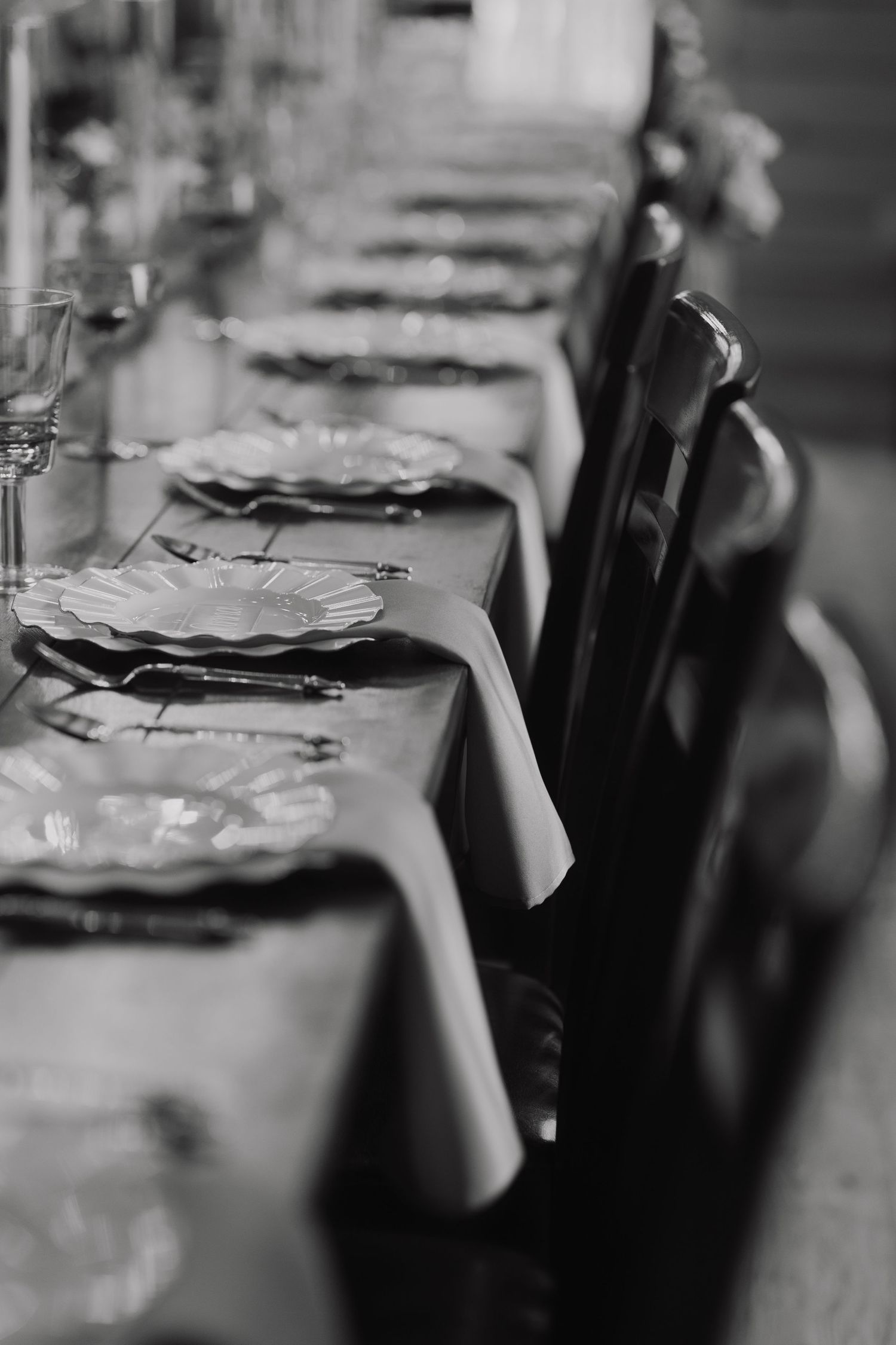 Elegant place settings with white plates arranged on long dining table in black and white.
