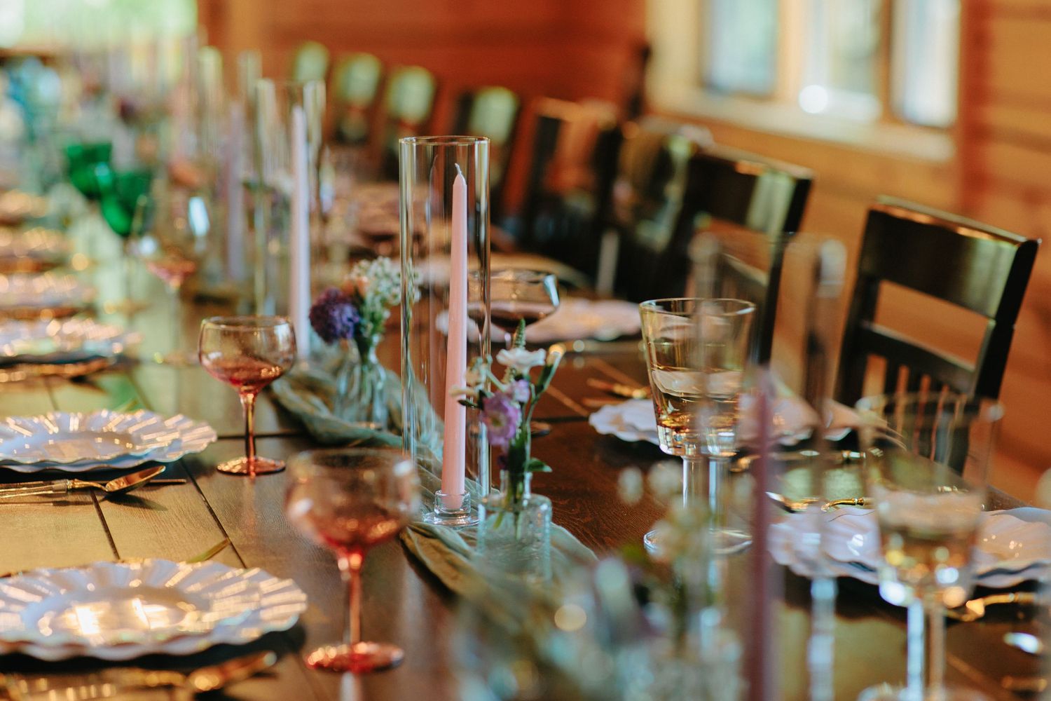 Elegantly set wedding reception table with wine glasses and candlesticks in rustic wooden venue.