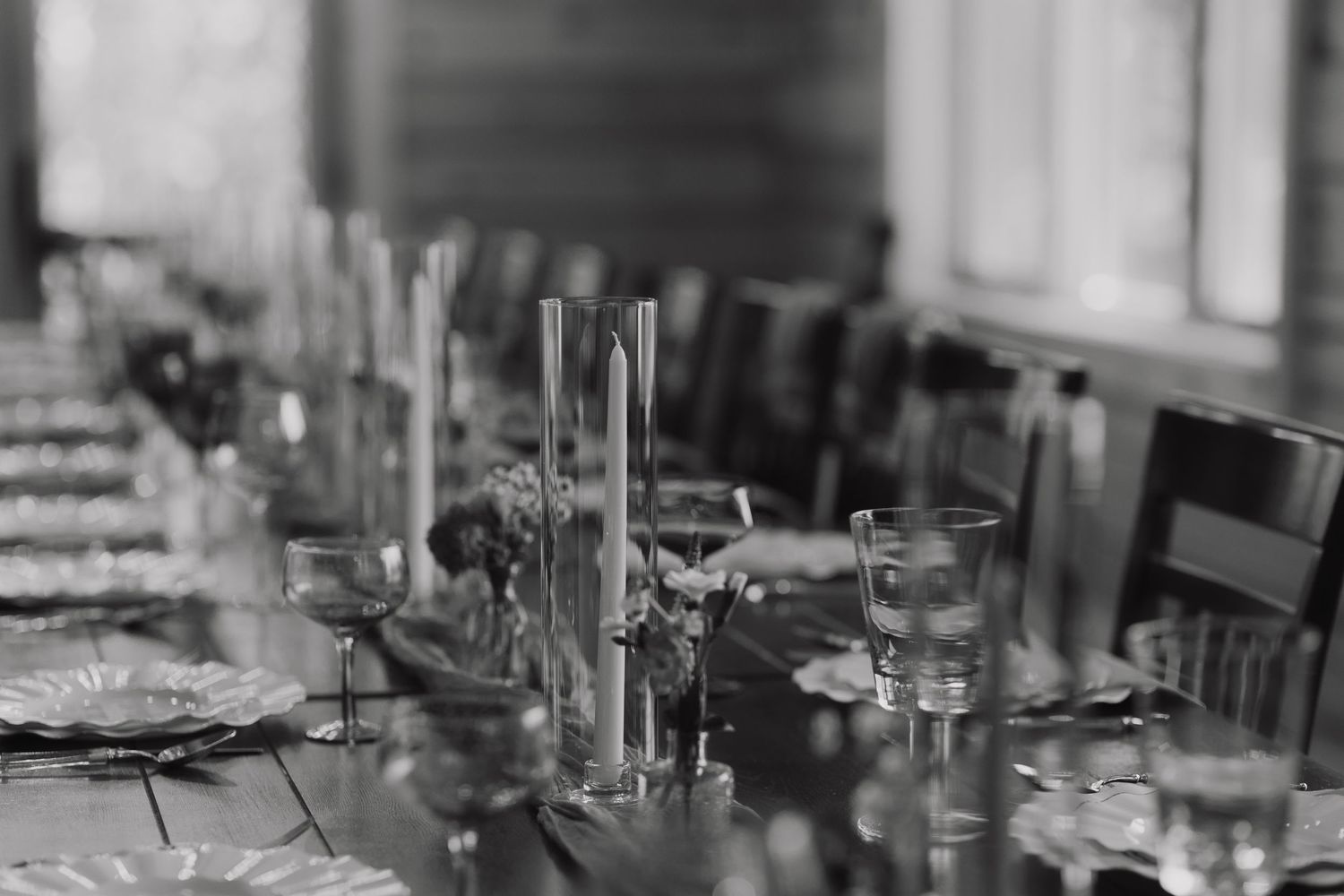 Wedding reception table settings with glassware and candles in moody lighting.