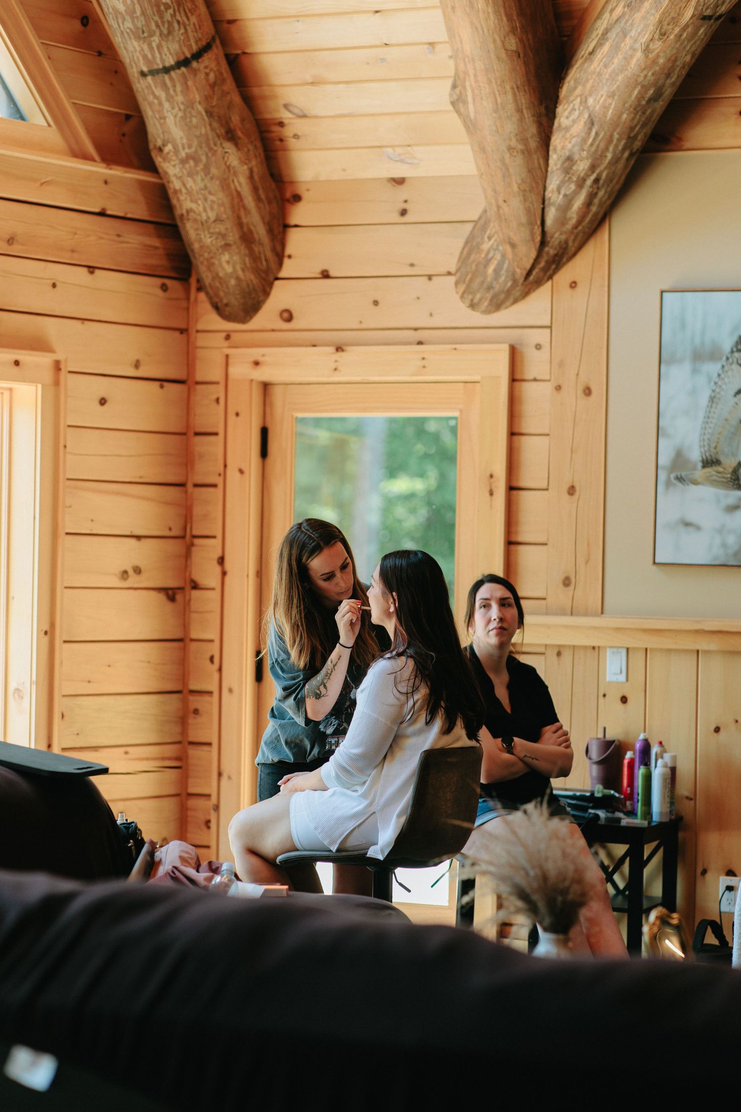 Wedding day preparation scene showing beauty services being performed in a log cabin interior.