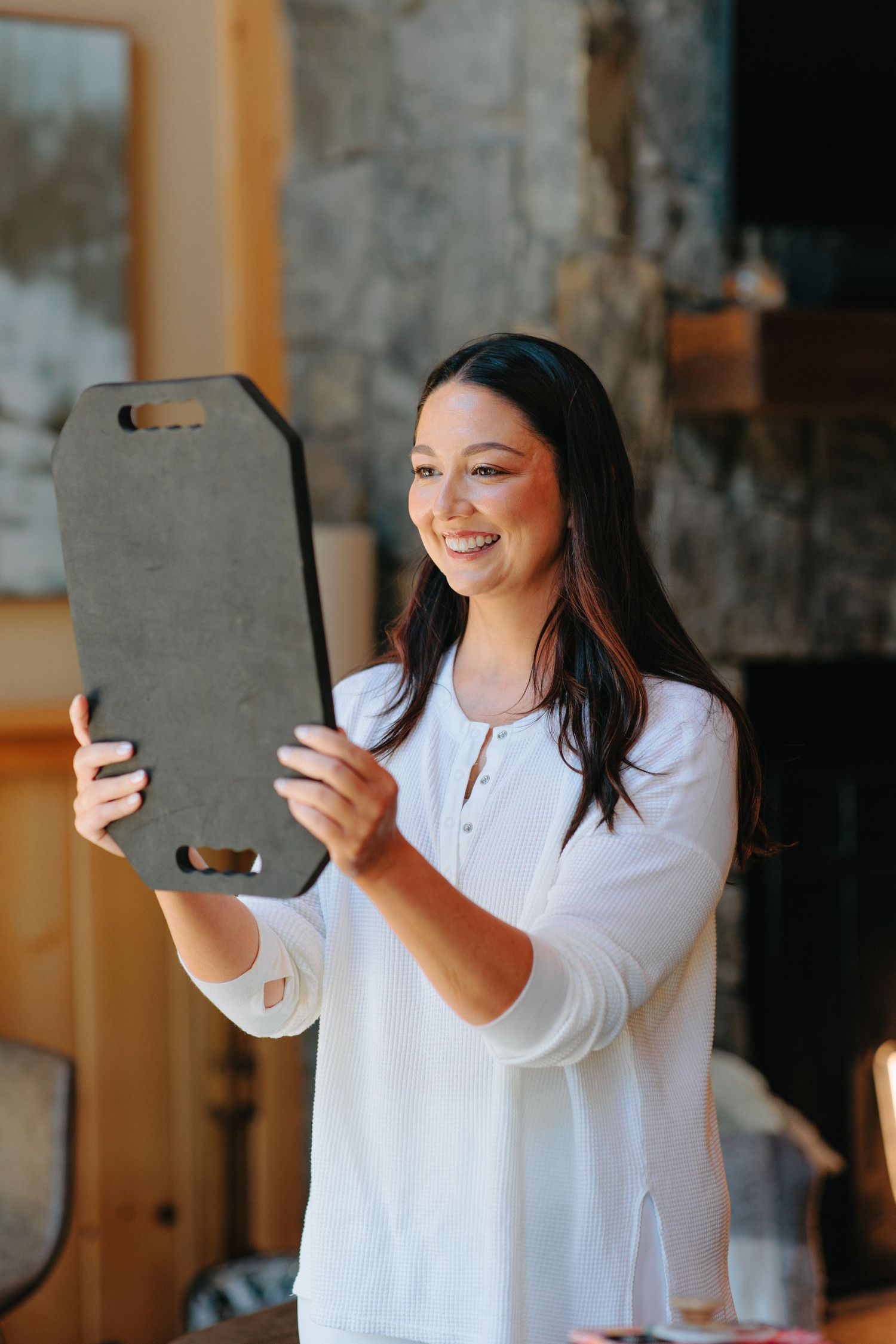 Person in white blouse smiling while holding a gray clipboard indoors.